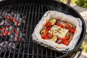 Fertiges geöffnetes Feta-Gemüse-Päckchen mit weicher Paprika und Zucchini in der indirekten Grillzone