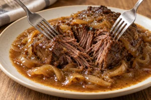 Zwei Gabeln teilen ein zartes Stück Rinderschmorbraten mit Zwiebeln und brauner Sauce