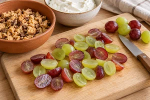 Halbierte rote und grüne Trauben auf einem Holzbrett neben Quark und groben Cookiebröseln