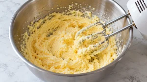 Helle Butter-Ei-Masse in einer Rührschüssel neben einem Handmixer